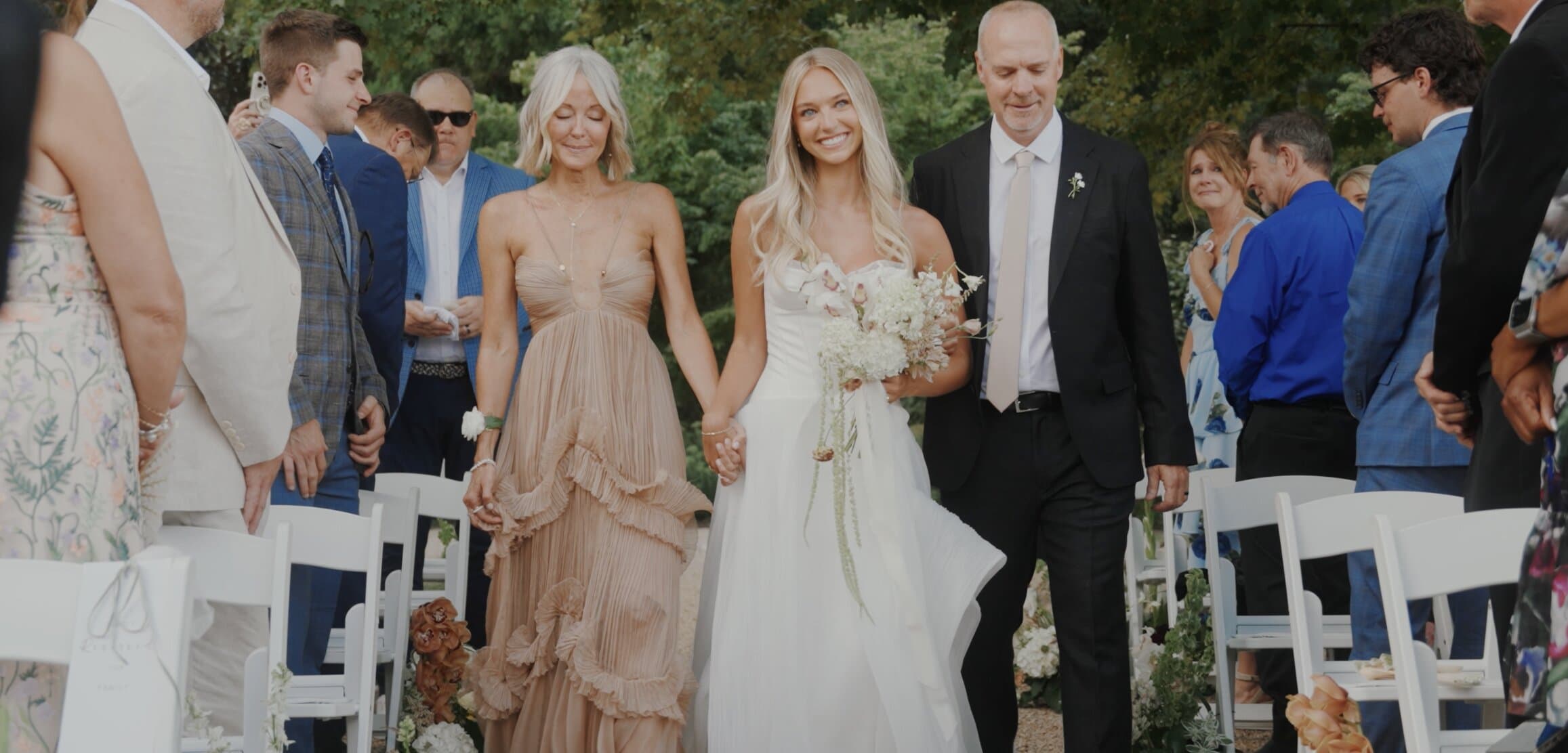 A bride walking down a garden aisle with her parents