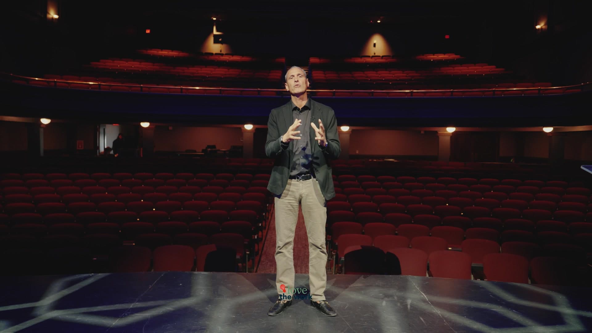 Dr. Nathan Unruh speaking on a theater stage during an event film